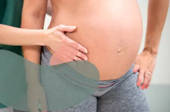 En hånd palperer magen til en gravid person